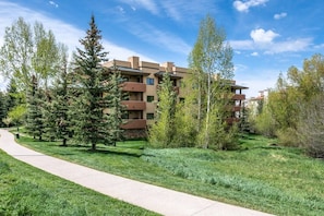 A residential building with multiple balconies, surrounded by a grassy area with trees.