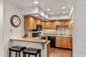 A modern kitchen with wooden cabinets, a central island with stools, a microwave, stove, and dishwasher.