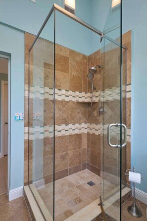 Une douche fermée par des parois de verre, avec un sol et des murs carrelés, une douchette à main et un porte-serviettes.