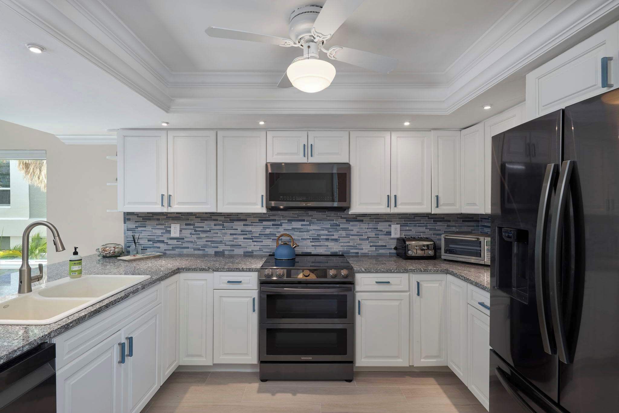 A modern kitchen with white cabinets, a stainless steel refrigerator, a microwave, and a stove.