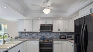 A modern kitchen with white cabinets, a stainless steel refrigerator, a microwave, and a stove. - St. Croix Four | Gorgeous Beachfront Townhome | Sun, Sand & Sea (Sanibel)