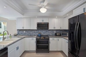 A modern kitchen with white cabinets, a stainless steel refrigerator, a microwave, and a stove.
