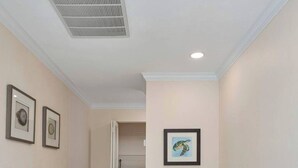 A hallway with a laundry area, a vent on the ceiling, and framed artwork on the walls. - St. Croix Four | Gorgeous Beachfront Townhome | Sun, Sand & Sea (Sanibel)