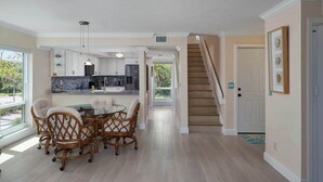 A spacious kitchen with modern appliances, a dining area with wicker chairs, and a staircase leading to another level. - St. Croix Four | Gorgeous Beachfront Townhome | Sun, Sand & Sea (Sanibel)