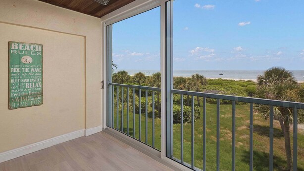 A balcony with a view of the ocean, a ceiling fan, and a wall with a 'Beach Rules' sign. - St. Croix Four | Gorgeous Beachfront Townhome | Sun, Sand & Sea (Sanibel)