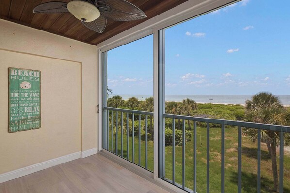 Un balcon avec vue sur l’océan, un ventilateur de plafond et un mur orné d’un panneau indiquant les règles à respecter sur la plage.