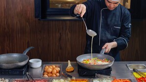 Een kok kookt in een keuken met diverse ingrediënten en keukengerei.