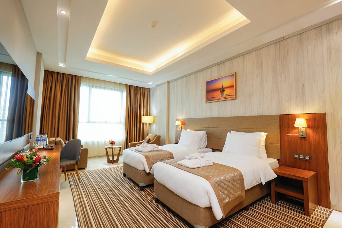 A hotel room with two beds, a desk with a vase of flowers, a chair, a TV, and a painting on the wall.