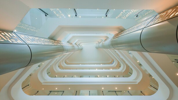 Een meerlaags atrium met een wenteltrap in het midden en glazen balustrades.