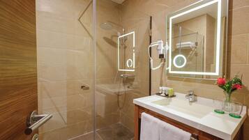 Casa de banho moderna com cabine de chuveiro em vidro, toucador com espelho e um vaso com flores.