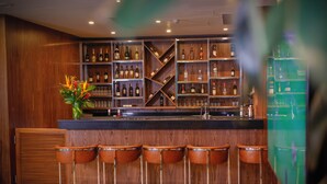 Een bar met houten schappen vol flessen, een bar en vijf krukken.