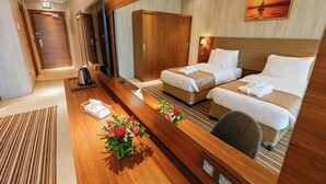 Een hotelkamer met twee bedden, een houten bureau, een spiegel, een schilderij van een zonsondergang en een bloemstuk.