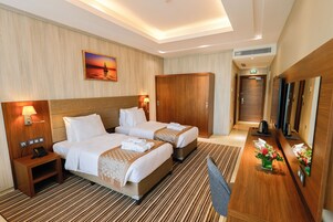 Una habitación de hotel con dos camas, un armario de madera, una mesita de noche con lámpara, una pequeña mesa con teléfono y un espejo decorado con un arreglo floral.