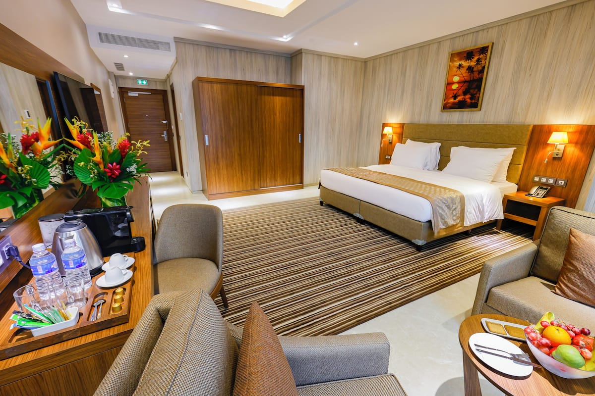 A hotel room with a bed, a sofa, a dining area with a tray of breakfast items, and a large artwork on the wall.
