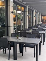 Moderni ulkotila, jossa on useita pöytiä ja tuoleja, suuret ikkunat ja näkymä ulkoalueelle.