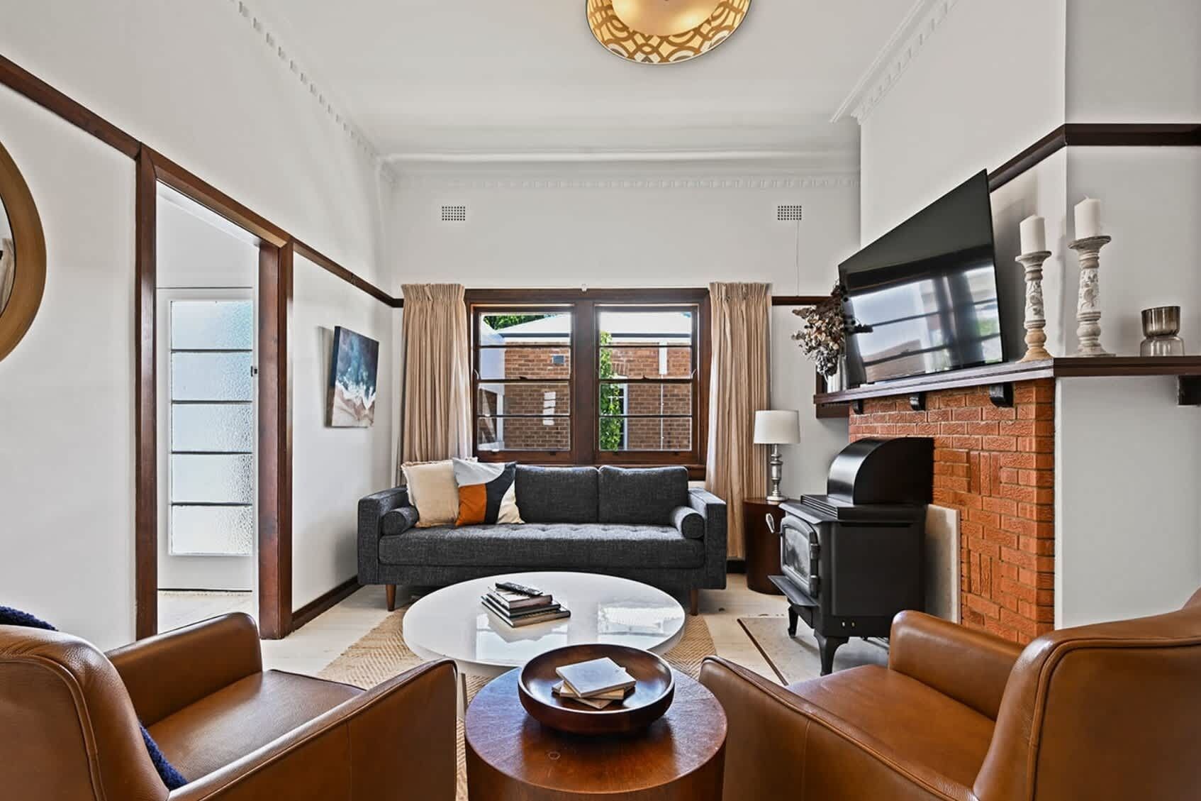 A living room with a sofa, coffee table, and leather chairs. There is a fireplace, a TV, and a window with curtains.