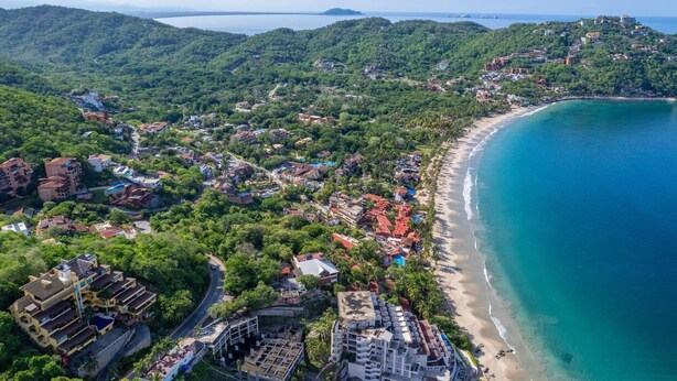 An aerial view of a coastal town with a beach, residential buildings, and a mountainous backdrop. - Best Views of Zihua 3Bed 3 Bath luxury (Zihuatanejo)