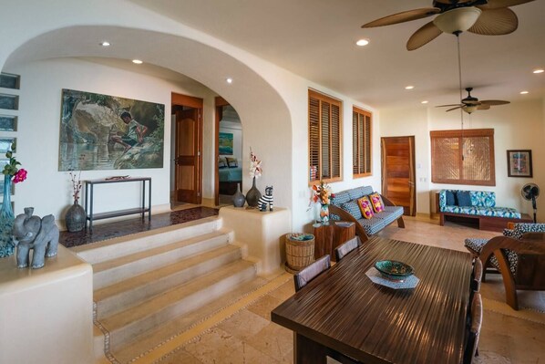 A spacious living area with a wooden dining table, a sofa, and a staircase leading to another room. - Best Views of Zihua 3Bed 3 Bath luxury (Zihuatanejo)