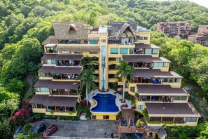 A multi-story hotel with a central pool, surrounded by lush greenery and multiple balconies.