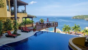 A pool with a view of the ocean, lounge chairs, and a wooden deck overlooking the sea. - Best Views of Zihua 3Bed 3 Bath luxury (Zihuatanejo)