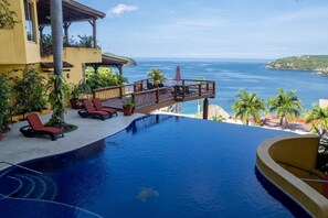 A pool with a view of the ocean, lounge chairs, and a wooden deck overlooking the sea. - Best Views of Zihua 3Bed 3 Bath luxury (Zihuatanejo)