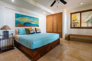 A bedroom with a bed, a painting, a wardrobe, a bench, and a window with blinds.