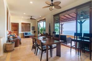 A dining area with a large table and chairs, a ceiling fan, and a view of the ocean. - Best Views of Zihua 3Bed 3 Bath luxury (Zihuatanejo)