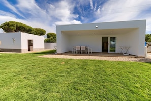 A modern house with a white exterior, a covered patio with a table and chairs, and a well-maintained lawn.