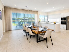 Una cocina moderna con armarios blancos, un refrigerador de acero inoxidable y un comedor con mesa y sillas de madera.