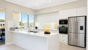 Una cocina moderna con armarios blancos, un refrigerador de acero inoxidable y una isla grande con un lavamanos.
