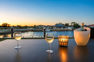 Mesa junto al agua con dos copas de vino blanco y un candelabro con vela encendida.