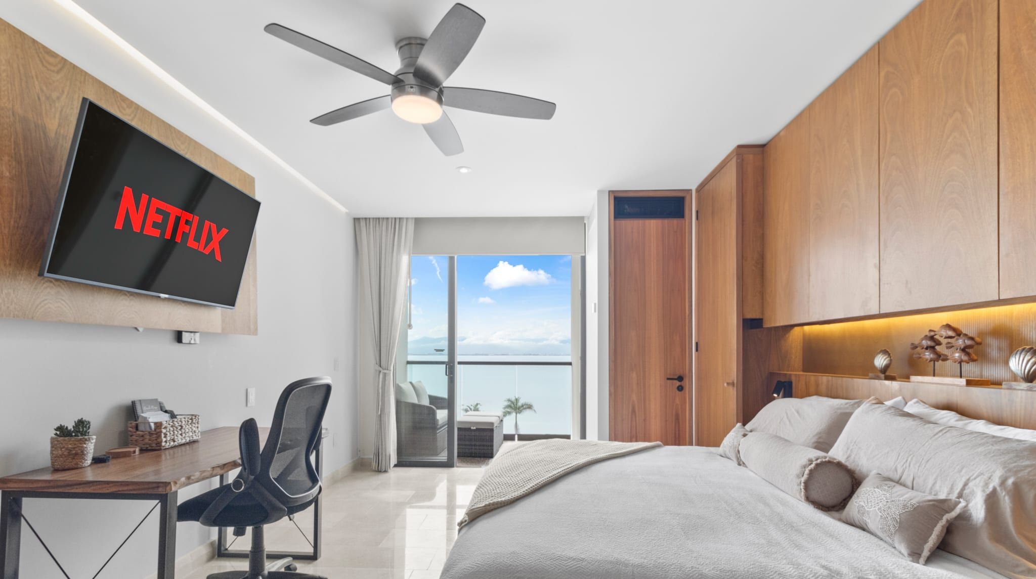 Habitación de hotel moderna con cama, escritorio, silla, televisor y ventilador de techo.