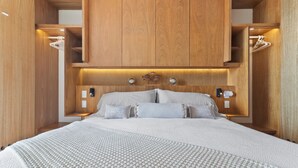 A modern bedroom with a large bed, wooden headboard, built-in shelving, and wall-mounted lighting. - Zantamar 307B: Beachfront Suites w Ocean Views (Cruz de Huanacaxtle)
