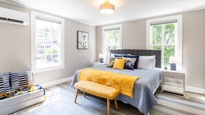 A bedroom with a bed, bench, bedside tables, and large windows.