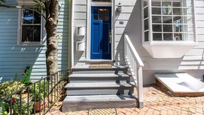 A two-story house with a blue front door, a small porch, and a brick pathway leading to the door.