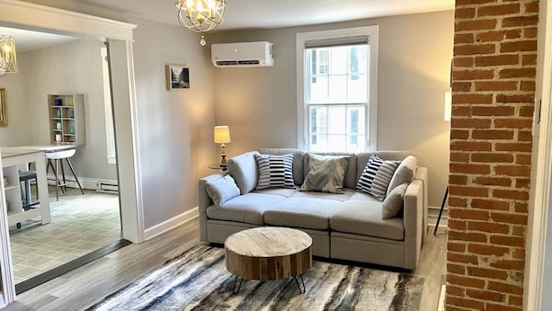 A living room with a grey sofa, a round wooden coffee table, and a striped rug.