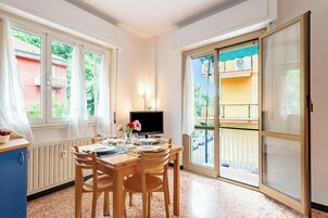 A dining area with a table, chairs, a TV, and a view of a balcony.