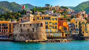A coastal town with colorful buildings, a prominent stone tower, and a flag. - Beautiful Flat in Rapallo (Rapallo)