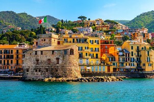 A coastal town with colorful buildings, a prominent stone tower, and a flag.