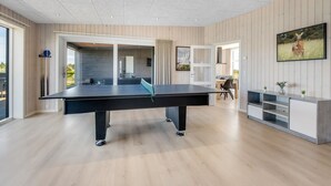 Spazio interno moderno con tavolo da ping pong, zona pranzo e TV a parete.