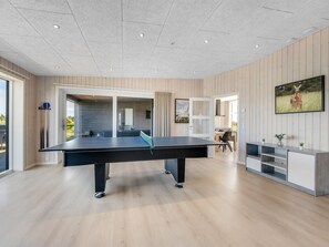 A modern indoor space with a ping pong table, a dining area, and a TV mounted on the wall.