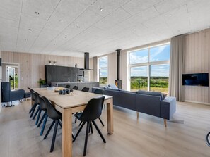 A modern kitchen with a dining area, large windows, and a flat-screen TV.