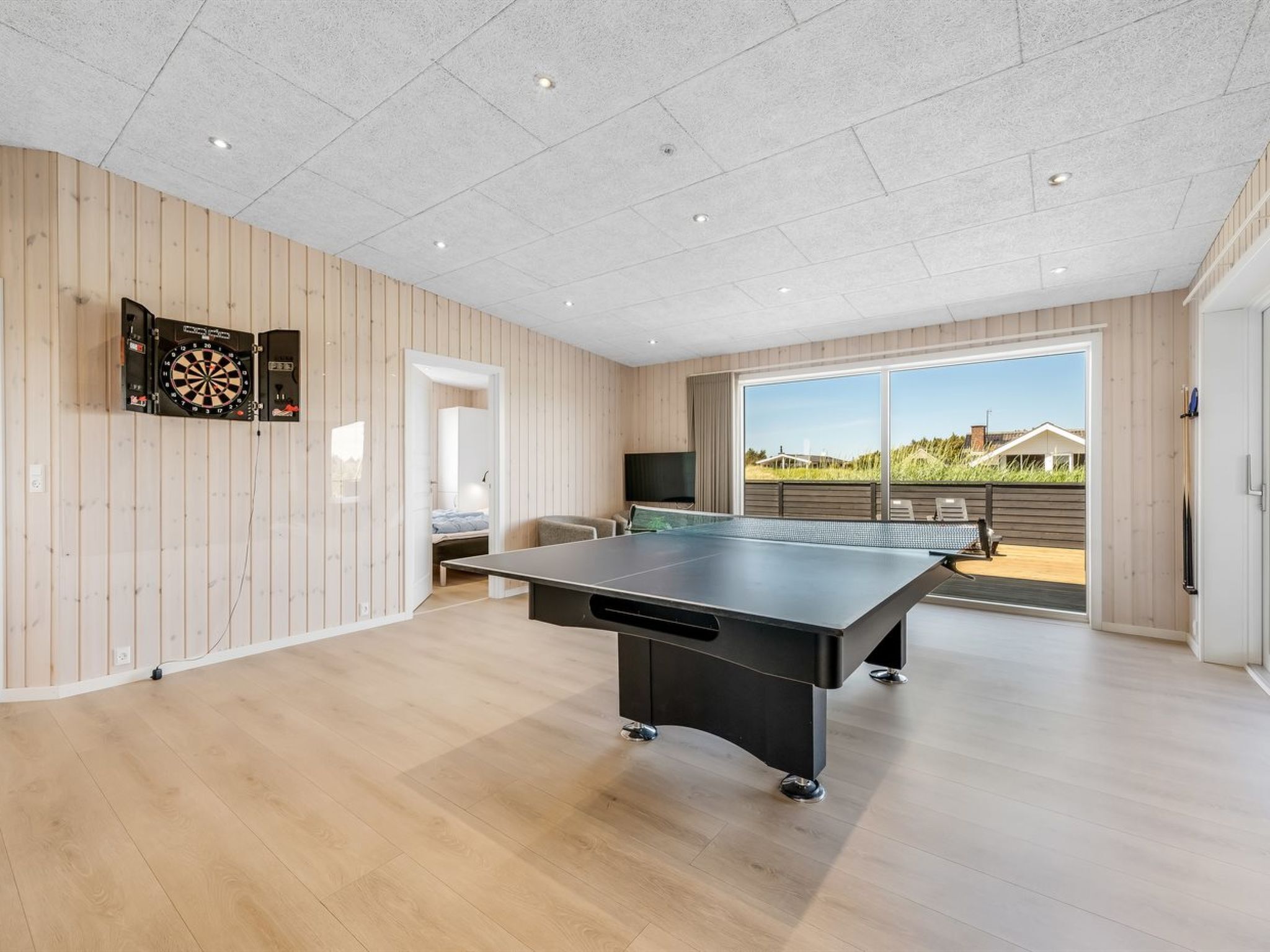 Una habitación con mesa de ping pong, dardos y televisión.