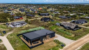 Una vista aerea di una zona residenziale con case moderne, tra cui una casa nera in evidenza con un'ampia terrazza, e una strada sterrata.