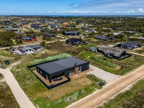 An aerial view of a residential area with modern houses, a prominent black house with a large deck, and a dirt road.