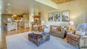 A spacious living area with a wooden ceiling, a leather sofa, a coffee table, and a kitchen in the background.