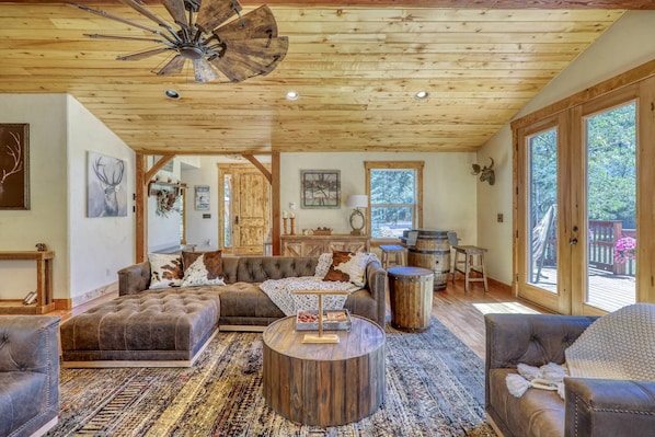 A spacious living room with a large sofa, a round coffee table, and a ceiling fan. There is a wooden dining table and chairs in the background.