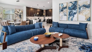 A modern living room with a blue sofa set, a wooden coffee table, and abstract wall art. - Vor4632td: 7 Bed, Bricktopia, Petting Zoo, Gaming Nook (Orlando)