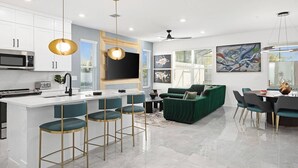 A modern kitchen with a central island, bar stools, a green sofa, and a dining area with chairs and a table. - Vor4784hw: 5 Bed, Candy Land, Pool (Orlando)