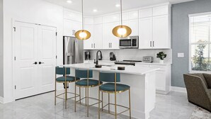 A modern kitchen with white cabinetry, a central island with bar stools, stainless steel appliances, and pendant lighting. - Vor4784hw: 5 Bed, Candy Land, Pool (Orlando)